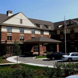 A view of a multi-story brick building with a driveway and parked cars at the entrance.