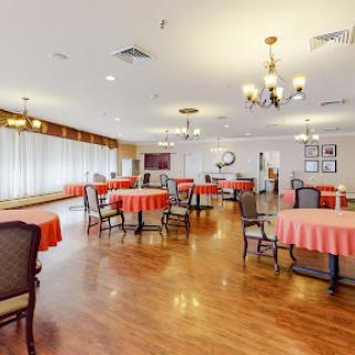 An inviting dining area featuring well-arranged tables with red tablecloths, surrounded by comfortable chairs and warm lighting.