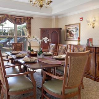 A well-decorated dining room featuring a large table surrounded by chairs, with elegant decor including a chandelier and orchids.