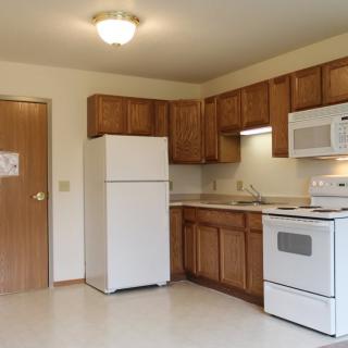 A simple kitchen with wooden cabinets and basic appliances including a refrigerator, stove, and microwave.