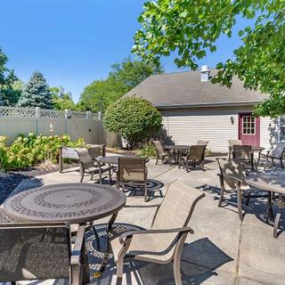 A sunny outdoor patio with tables and chairs surrounded by greenery.