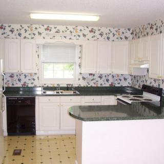 A traditional kitchen interior with white cabinets and floral wallpaper.