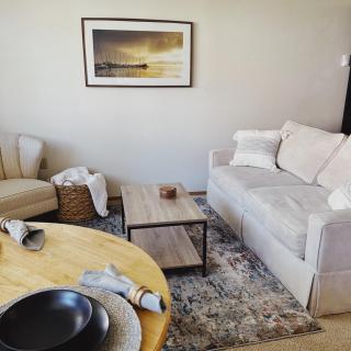 A cozy living room with a minimalist design, featuring a white sofa, a comfortable chair, and a wooden coffee table.