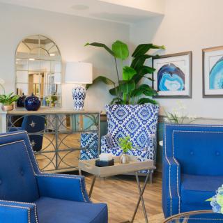 A stylish living room featuring blue armchairs and geometric patterned accents, enhanced by modern artwork and lush greenery.