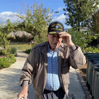 A man walking outdoors on a sunny day, wearing a hat and jacket.