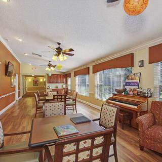 A cozy living room with a dining area, featuring a piano and ample natural light from large windows.