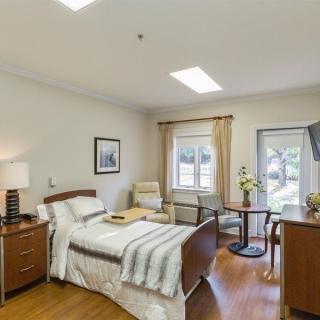 A comfortable hospital room featuring a neatly made bed, a chair by the window, and a television opposite the bed.