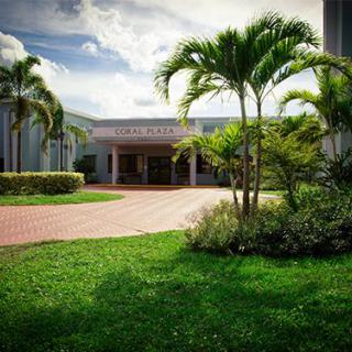 A serene building entrance surrounded by palm trees and greenery under a partly cloudy sky.