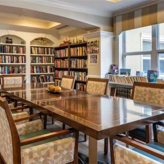 A cozy library reading room with a large wooden table surrounded by comfortable chairs and shelves filled with books.