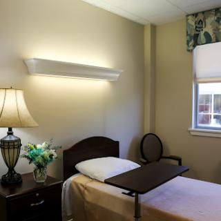 A well-lit hospital room featuring a bed with a bedside table, lamp, and decorative flowers.