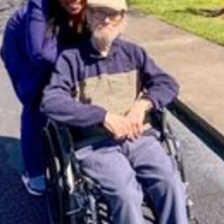 An elderly person in a wheelchair enjoying a sunny day outdoors with a companion.