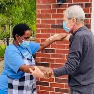 Two people wearing masks engage in a friendly greeting outdoors near a brick wall.