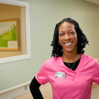 A healthcare professional smiling in a pink uniform, exuding warmth and approachability.