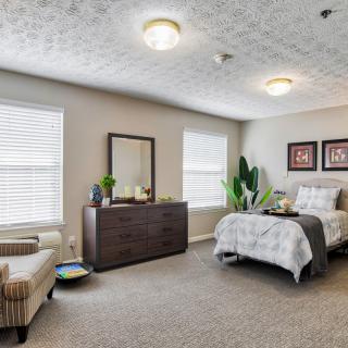 A modern and cozy bedroom featuring a neatly made bed, dresser, armchair, and stylish decor.