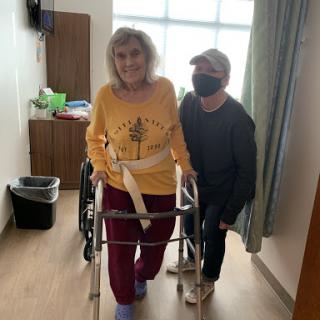 A caregiver assists an elderly person using a walker in a rehabilitation setting.