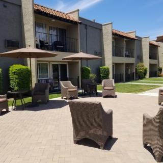 A sunny outdoor patio area with wicker chairs and umbrellas in front of an apartment building.