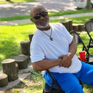 A man enjoying a sunny day at the park, dressed casually and relaxing on a chair.