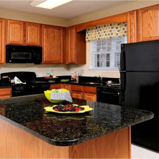 A modern kitchen with wooden cabinets and black appliances, featuring a central island with a dark countertop.