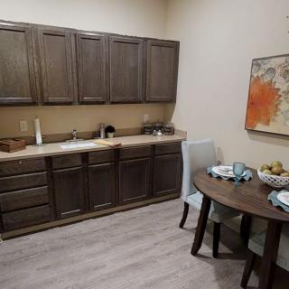 A cozy kitchen area featuring wooden cabinets, a sink, and a small dining table set with chairs and artwork on the wall.