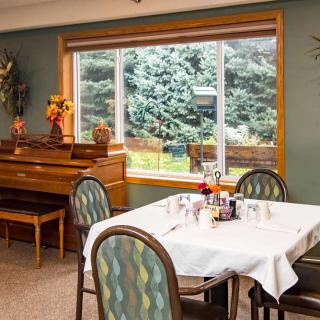 A cozy dining area with a table set for a meal, complemented by a piano and large window providing natural light.