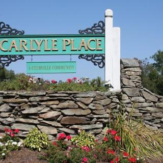 A decorative entrance sign for Carlyle Place set against a stone wall with blooming flowers.
