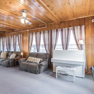 A cozy living room with wood paneling, featuring a white piano and comfortable seating.