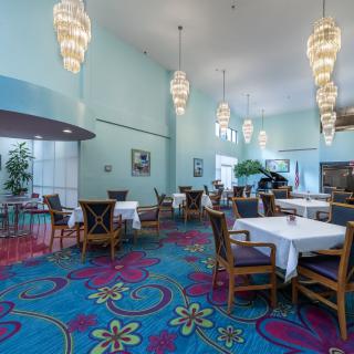 A vibrant restaurant interior with colorful carpeting, elegant chandeliers, and neatly arranged tables and chairs.