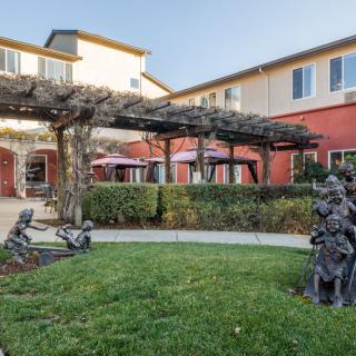 A quaint garden area featuring sculptures, surrounded by a multi-story building with a pergola.