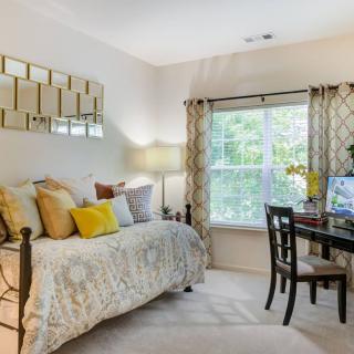 A cozy bedroom with a decorative daybed, desk setup by the window, and accent decor.