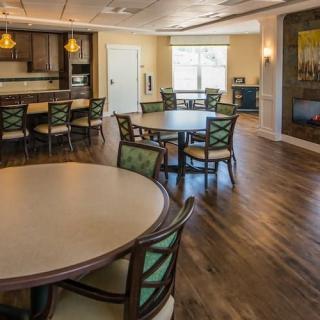 A spacious dining area with round tables and chairs, featuring a kitchen in the background and wooden flooring.