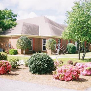 A well-maintained brick house surrounded by a landscaped garden with various shrubs, bushes, and trees.