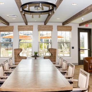 A modern conference room with a large meeting table and chairs, featuring ample natural light through several windows.