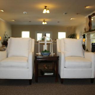 A cozy living room with two white chairs and a small wooden table under warm lighting.
