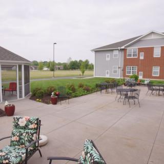 A spacious outdoor patio with seating and tables, adjacent to a building and landscaped lawn.