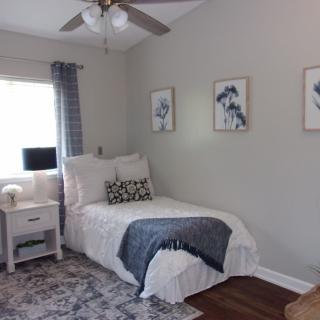 A cozy and well-decorated bedroom with a single bed, featuring neutral tones, artistic wall decor, a rug, and a bedside table.