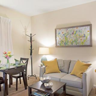 A cozy living room with a dining area, featuring a sofa, decorative pillows, artwork on the wall, and a well-set table.