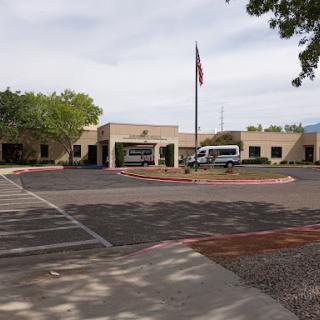 A view of a building with a flagpole and parked vehicles in the foreground.