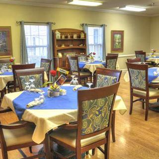A neatly arranged dining room with tables set for a formal meal, featuring blue and beige tablecloths and decorative elements.
