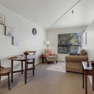 A cozy living room with a small dining area, featuring an armchair and sofa next to a large window.