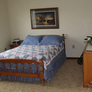 A cozy bedroom with a wooden bed frame, blue bedding, and a painting on the wall.