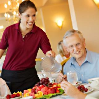 A server pouring water for an elderly man at a restaurant.
