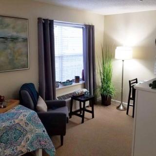 A cozy bedroom with a bed, chair, lamp, and indoor plant by the window.