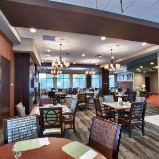 A spacious and well-lit restaurant dining area with elegantly arranged tables and chairs, complemented by modern chandeliers.