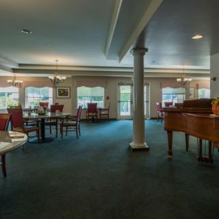 A spacious lounge area featuring a piano, dining tables, and chairs with large windows letting in natural light.
