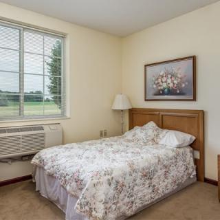 A simple and cozy bedroom with a single bed, window, and artwork on the wall.