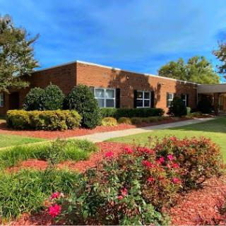 A well-maintained building surrounded by vibrant flowers and lush greenery under a clear blue sky.