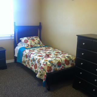 A cozy bedroom featuring a single bed with floral bedding and a matching dresser.