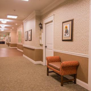 A well-lit hallway featuring an orange chair and framed artwork on the walls.