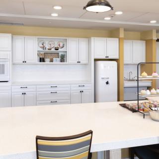 A modern kitchen with white cabinets and a large island countertop, featuring stylish lighting and minimalistic decor.