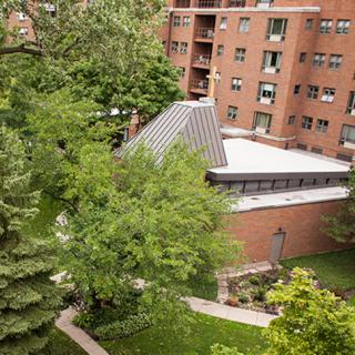 A view of a brick building surrounded by lush greenery and trees in an urban setting.